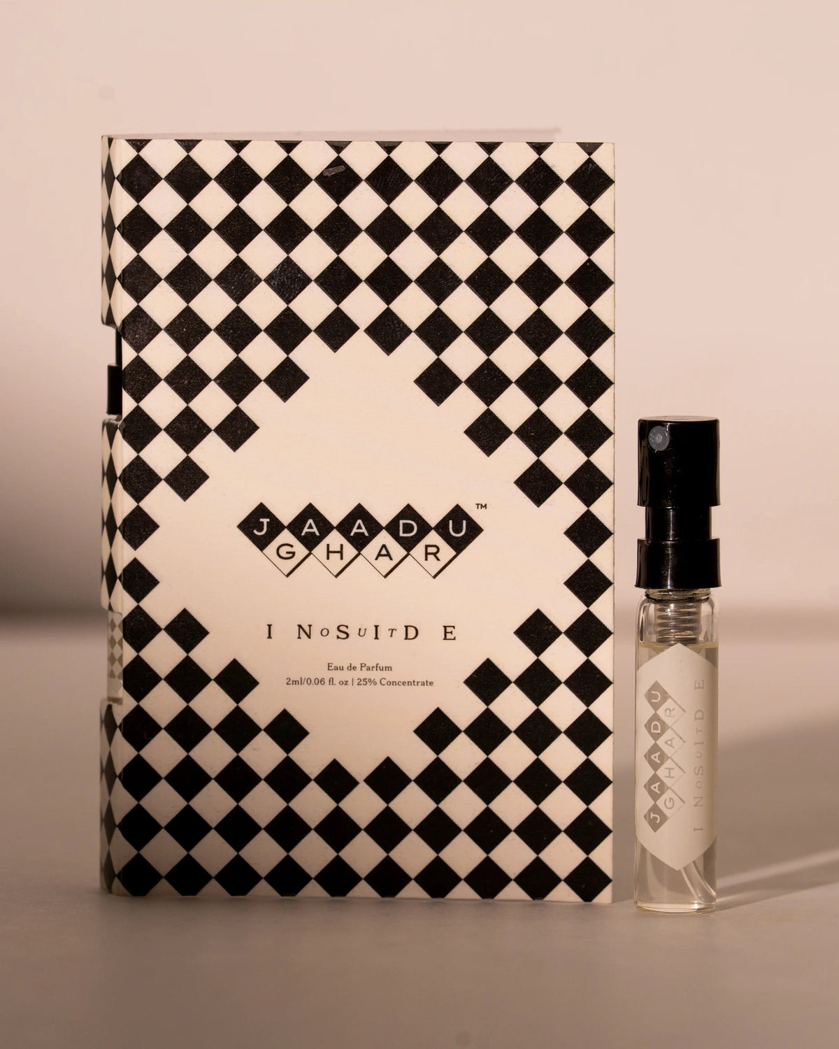 A small clear perfume spray bottle with a black atomizer cap stands beside its matching rectangular box. The packaging features a bold black and off-white diamond checkerboard pattern, with the brand name 'JAADU GHAR' and product name 'INSIDE OUT' printed in the center.